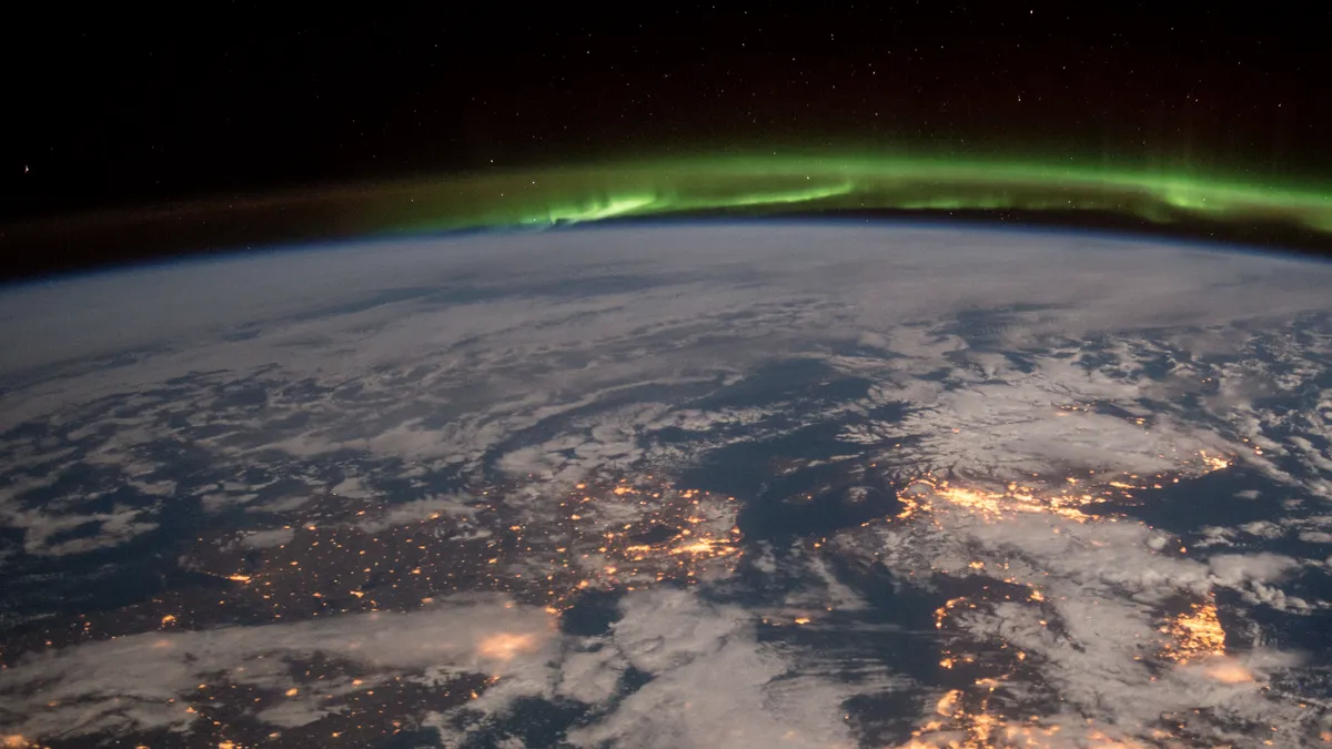 Nordlys over Nord-Europa om natten, bylys under et grønt bånd, sett fra Den internasjonale romstasjonen